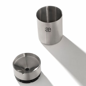 May include: A stainless steel coffee grinder with a funnel and a removable container. The container has the letters "ae" printed on it.