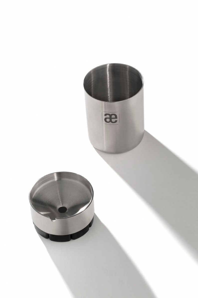 May include: A stainless steel coffee grinder with a funnel and a removable container. The container has the letters "ae" printed on it.