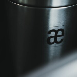 May include: Close-up of a stainless steel container with the letters "ae" printed on the side.