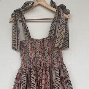 May include: A tiered maxi dress with a brown, pink, and blue geometric print. The dress has a smocked bodice and tie straps.