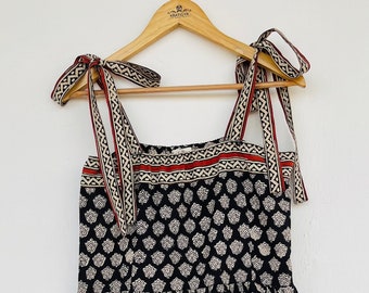 May include: A black and white patterned midi dress with red trim. The dress has a square neckline and thin straps that tie at the shoulders.