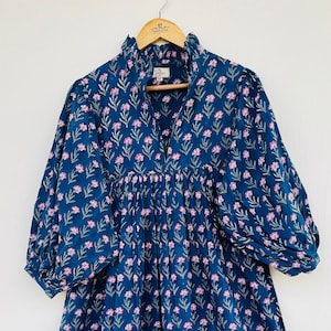 May include: A blue cotton dress with a pink floral print and a ruffled collar. The dress has a gathered waist and 3/4 sleeves.
