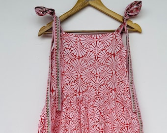 May include: A pink and red sleeveless dress with a white floral pattern. The dress has thin straps that tie at the shoulders.