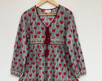Peut inclure: Robe longue à manches longues et à volants avec un col en V. La robe présente un fond bleu sarcelle clair avec un motif répété de motifs floraux rouges. L'encolure et les poignets sont bordés d'une bordure rouge foncé. Détail de pompon au col.