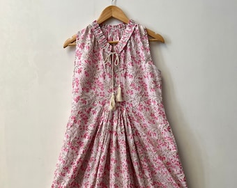 May include: A white sleeveless maxi dress with a pink floral print and a ruffled hem. The dress has a tie at the neckline and a tassel.