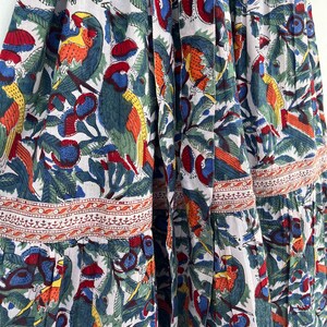May include: A white cotton dress with a colorful floral print featuring parrots, leaves, and berries. The dress has a tiered skirt and a fitted bodice.