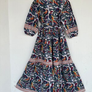 May include: A white maxi dress with a blue, green, and orange floral print featuring birds. The dress has a wrap style bodice and a tiered skirt.