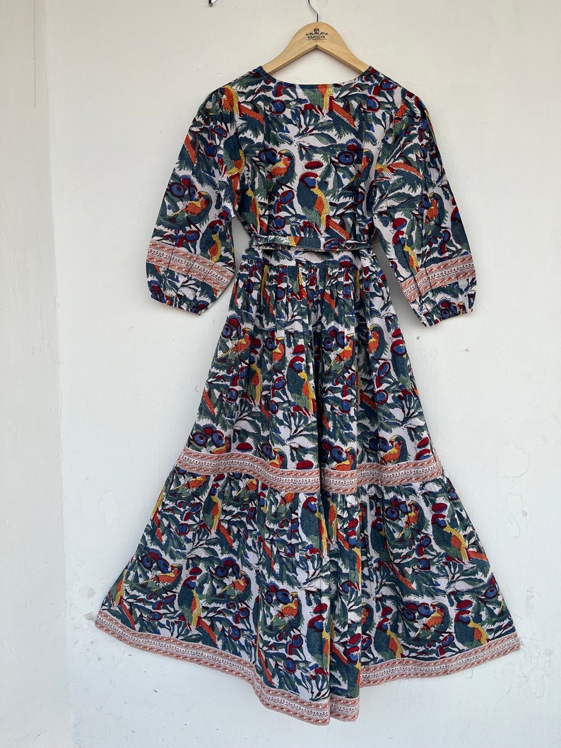 May include: A white maxi dress with a blue, green, and orange floral print featuring birds. The dress has a wrap style bodice and a tiered skirt.