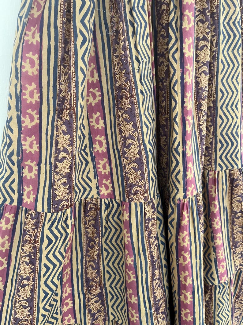 May include: A beige, pink, and blue striped fabric with a floral pattern. The fabric has a tiered design.