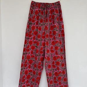 May include: Wide-leg pants with a pink background and a red floral print. The pants have an elastic waistband.