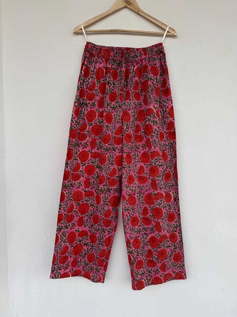 May include: Wide-leg pants with a pink background and a red floral print. The pants have an elastic waistband.