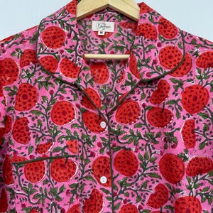 May include: A pink and red cotton shirt with a floral print. The shirt has a collar, button closure, and a pocket on the left side. The shirt is labeled with a size "M".