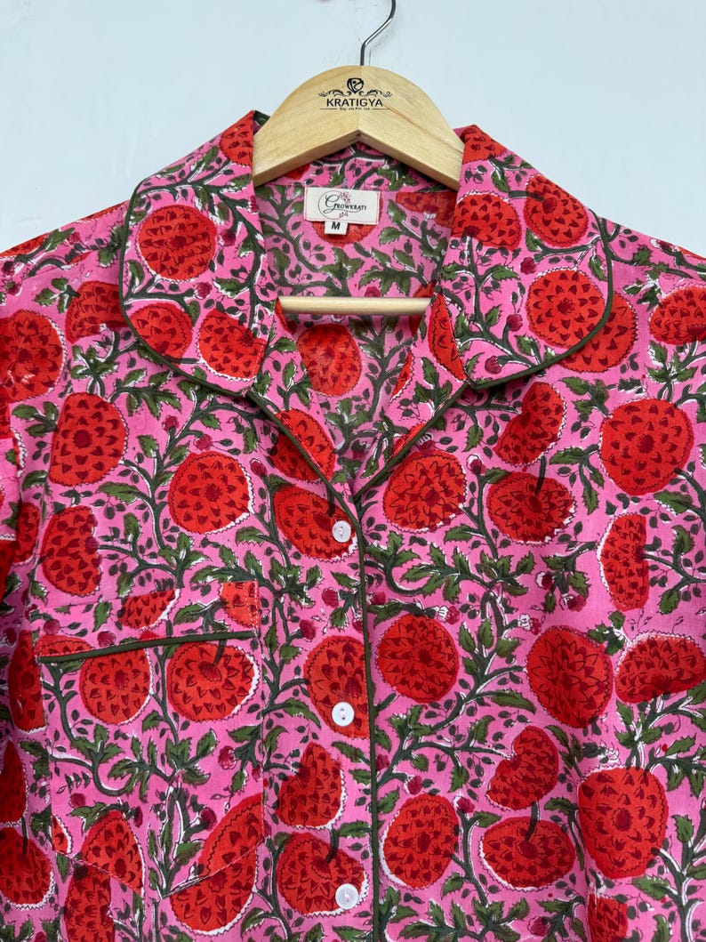 May include: A pink and red cotton shirt with a floral print. The shirt has a collar, button closure, and a pocket on the left side. The shirt is labeled with a size "M".