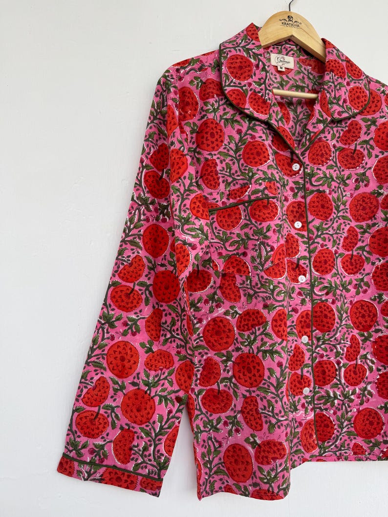 May include: A pink long-sleeved shirt with a red and green floral print. The shirt has a button-up front and a collar.