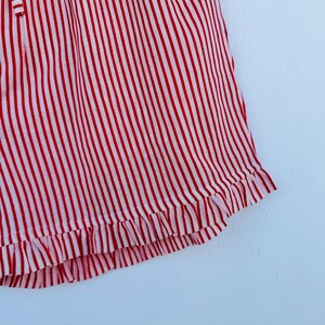 May include: Close-up of a red and white striped garment. The fabric has vertical stripes and a ruffled hem. The garment appears to be made of a lightweight material.