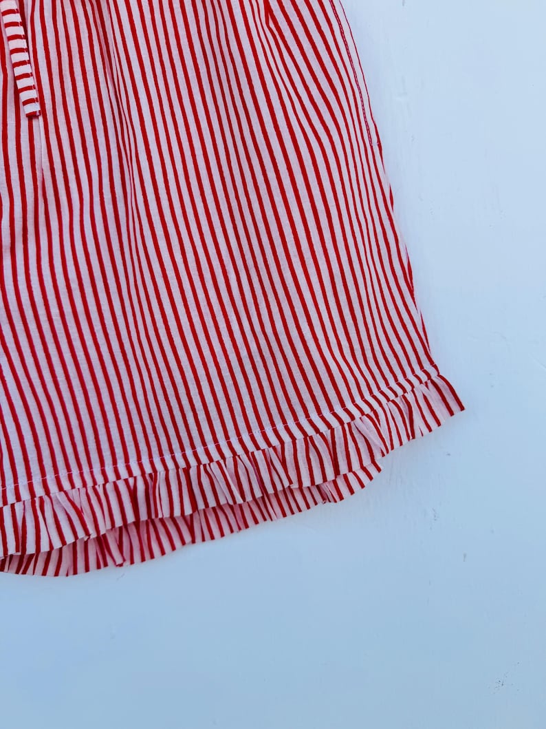 May include: Close-up of a red and white striped garment. The fabric has vertical stripes and a ruffled hem. The garment appears to be made of a lightweight material.