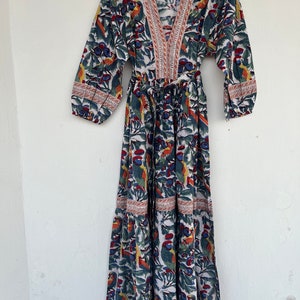May include: A white maxi dress with a colorful floral print featuring birds and leaves. The dress has a V-neckline, 3/4 sleeves, and a tie waist.