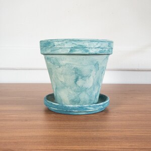 May include: A light blue terracotta planter with a distressed finish. The planter has a saucer.