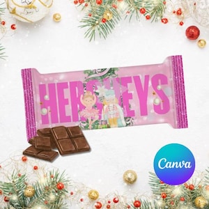 May include: A pink Hershey's chocolate bar with the word "HERSHEY'S" in large pink letters. The bar features a Christmas-themed design with a ballerina and a nutcracker. Several pieces of chocolate are in front of the bar.