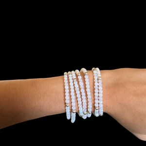 Könnte beinhalten: Ein Stapel weißer Perlenarmbänder mit silbernen Akzenten. Die Armbänder werden am Handgelenk getragen.