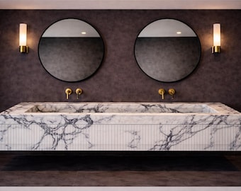 May include: A wall-mounted double vanity featuring a white marble countertop and basin with prominent dark grey veining. The front panel has a vertical fluted texture. Two round mirrors with thin black frames and two gold wall sconces are mounted above.