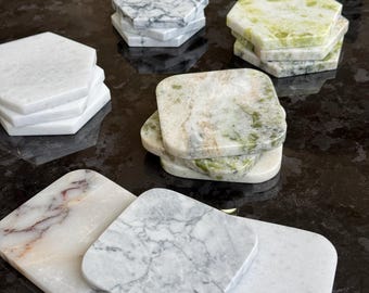 May include: A collection of stone coasters in various shapes and patterns. The set includes hexagonal white marble, green and white marbled stone, and square coasters featuring white, grey, and reddish-brown veining on polished stone surfaces.