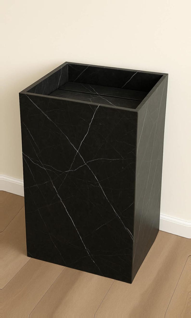 Puede incluir: Un pedestal rectangular alto con acabado negro y vetas blancas en toda la superficie. La estructura presenta un dise&ntilde;o hueco con la parte superior abierta y una base plana, mostrando una silueta geom&eacute;trica limpia con bordes definidos.