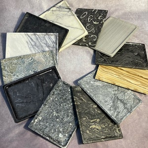 May include: A collection of 10 rectangular serving trays made of different types of stone, arranged in a circle on a light purple background.
