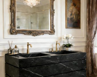 May include: A stylish bathroom interior featuring a black marble vanity unit with gold taps and a large ornate mirror. The mirror reflects a chandelier. The room also includes a painting and a curtain.
