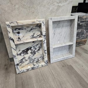 Puede incluir: Dos estantes empotrados de mármol. Uno tiene un patrón veteado blanco y negro, el otro es blanco. Ambos tienen un marco rectangular y un solo estante. Los estantes están sobre un suelo con aspecto de madera.