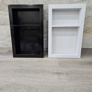 May include: Two bathroom shelves, one black and one white, with two shelves each. The shelves are mounted on a wall.