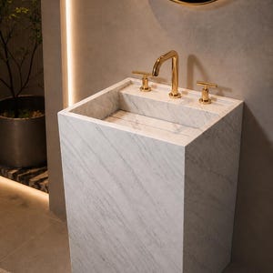 Puede incluir: Un lavabo de pedestal de m&aacute;rmol blanco independiente con un lavabo rectangular y un grifo de oro pulido con dos manijas en forma de T a juego. El lavabo presenta un patr&oacute;n de vetas grises en toda la superficie de piedra y un dise&ntilde;o angular.