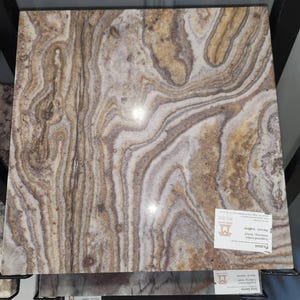 Könnte beinhalten: Eine rechteckige Platte aus Picasso-Marmor mit einem wirbelnden Muster aus Braun, Beige und Weiß. Der Stein hat eine polierte Oberfläche und wird auf einem Metallgestell ausgestellt. Das Etikett lautet "Picasso".