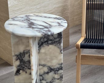 May include: A white marble side table with a round top and a unique, geometric base. The table has a light gray and purple marbling pattern.