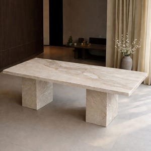 Puede incluir: Una mesa de comedor rectangular con una superficie de mármol beige pulido con vetas de color crema y marrón claro. La mesa se apoya sobre dos bases de pedestal rectangulares gruesas de mármol a juego, creando un aspecto sólido y uniforme.