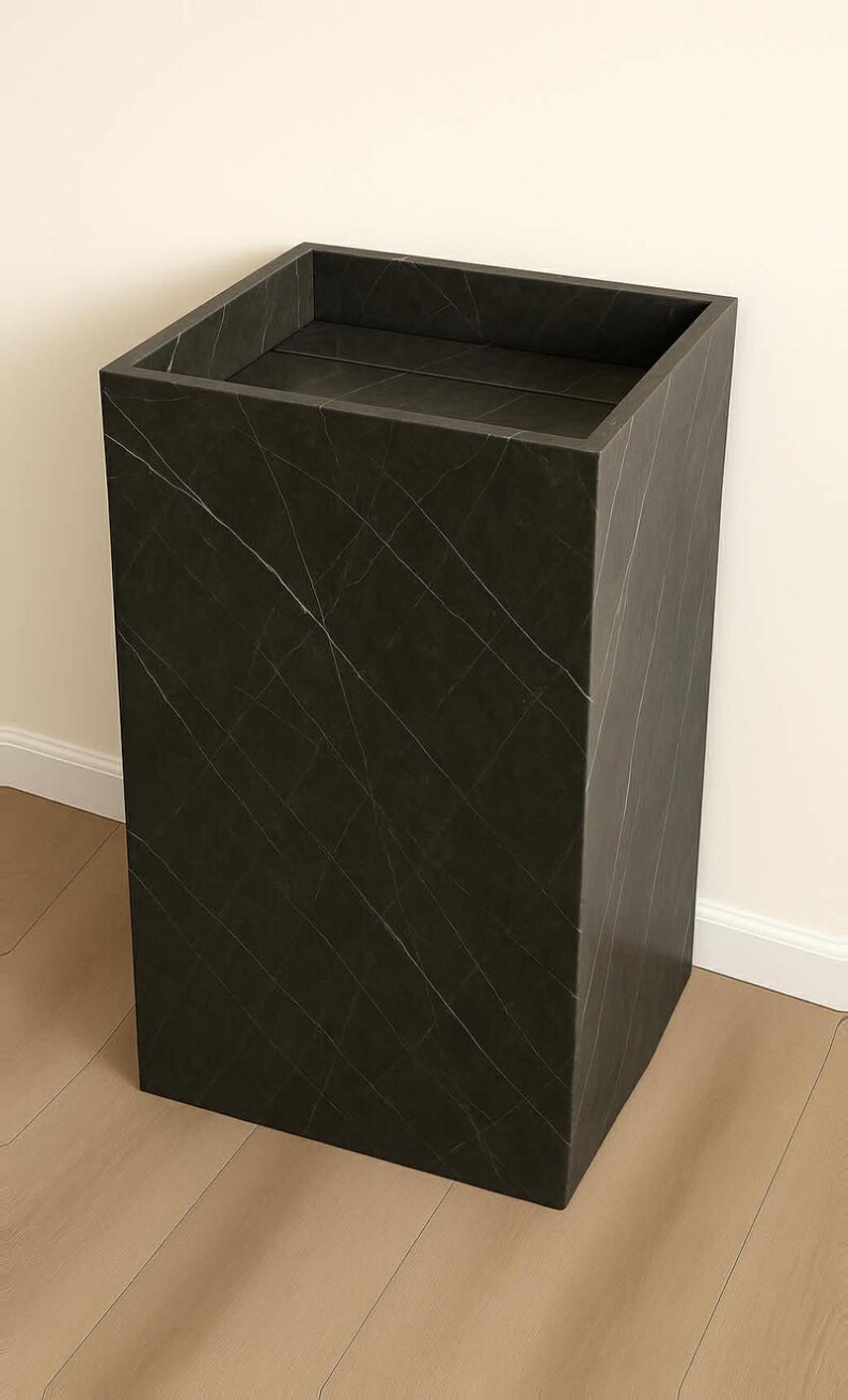 Puede incluir: Un pedestal o columna rectangular alta con un acabado gris carb&oacute;n oscuro que presenta vetas blancas finas y sutiles en toda la superficie. La estructura tiene una parte superior plana y abierta con bordes limpios y definidos.