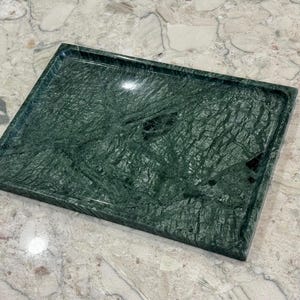 Peut inclure: Un plateau rectangulaire en marbre vert foncé avec une finition polie. Le plateau a un bord surélevé et un motif de veinage naturel. Le plateau convient au service ou à l'exposition.