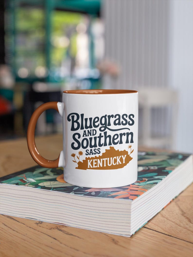 a coffee mug that says "bluegrass and southern sass Kentucky" with a kentucky and floral graphics. The design is part of A collection of Kentucky themed vector images perfect for cricut, silhouette, tshirt design, DTF Printing, POD, mugs, tote bags, sublimation and more!