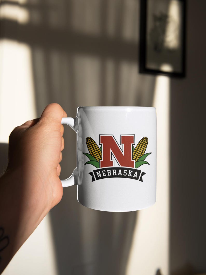 A white mug that says "nebraska" with an "N" graphic and two corn graphics