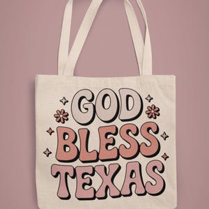 A white canvas tote bad that reads "god bless texas"