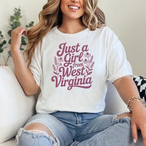a woman wearing a white tshirt that says "Just a girl from West Virginia" with floral graphics. this design is part of A collection of west virginia vector designs perfect for cricut, silhouette, sublimation, DTF Printing, POD, tshirts, mugs, tote bags and more!