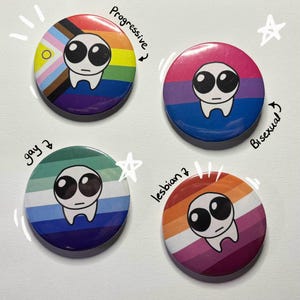 Puede incluir: Cuatro botones redondos con diferentes banderas del orgullo y una cara de extraterrestre de dibujos animados en cada uno. Las banderas están etiquetadas como "Progresivo", "Bisexual", "Gay" y "Lesbiana".