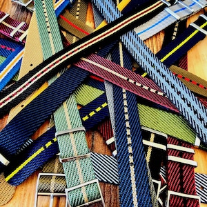 Pu&ograve; includere: Una collezione di cinturini colorati per orologi con vari disegni a righe e motivi. I cinturini sono in tonalit&agrave; di blu, verde, rosso e nero, con fibbie in metallo. I cinturini sono realizzati in tessuto intrecciato.