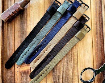 May include: Five different colored nylon watch straps with black metal buckles. The straps are arranged in a fan shape on a wooden surface.