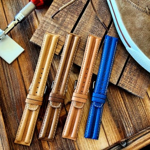 May include: Four leather watch straps in different colors, including brown, tan, and blue. The straps are laid out on a wooden surface.