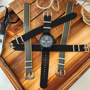 May include: A black watch with a black band and a white face. The watch is surrounded by four gray and yellow watch bands.