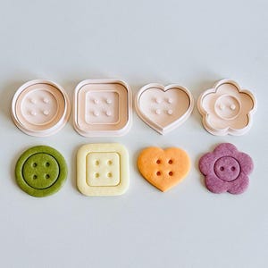 Peut inclure: Ensemble de découpoirs à biscuits et de biscuits en forme de boutons, de différentes formes et couleurs. Les découpoirs sont rose clair, tandis que les biscuits sont verts, jaunes, oranges et violets. Formes : cercles, carrés, cœurs et fleurs.