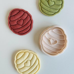 Pu&ograve; includere: Tre stampini per biscotti a forma di favo con un cuore al centro. Gli stampini sono verde, rosso e giallo. Gli stampini sono su uno sfondo grigio chiaro.