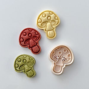 Peut inclure: Quatre emportes-pièces en forme de champignon, deux sont rouges, un est vert et un est blanc. L'emporte-pièce blanc est le plus grand et semble être le moule pour les trois autres.