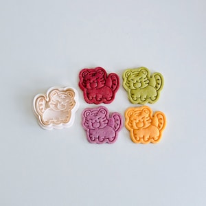 May include: Five cookie cutters in the shape of a tiger. The cutters are in various colors: red, green, purple, orange, and white.